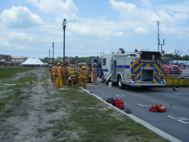 A group of firefighters in turnout gear gathered next to a fire engine